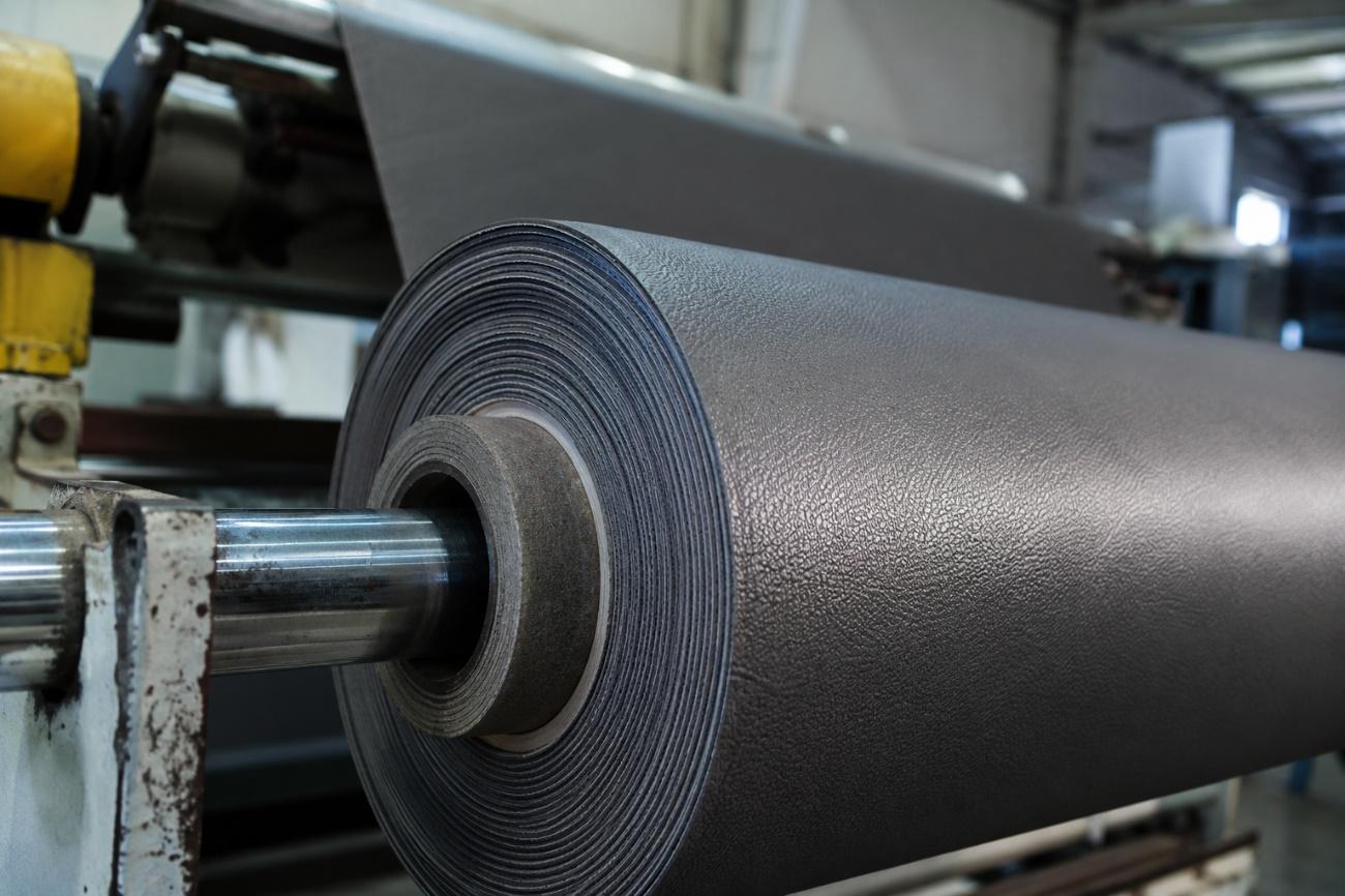 Rolo de revestimento sintético em PVC em linha industrial, simbolizando a qualidade e a trajetória da Agro Química São Gabriel S/A na fabricação de materiais.